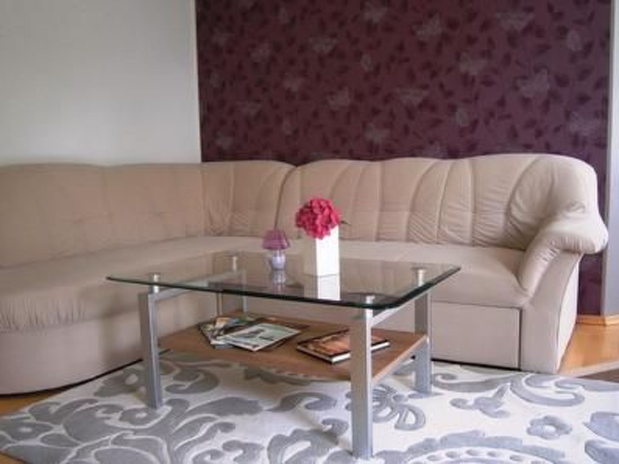 Un salon avec un canapé beige, une table basse en verre et un tapis à motifs floraux.