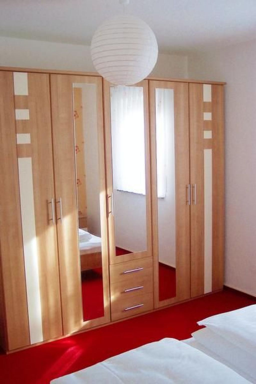 A bedroom with a large wardrobe, a bed, and a hanging light fixture.