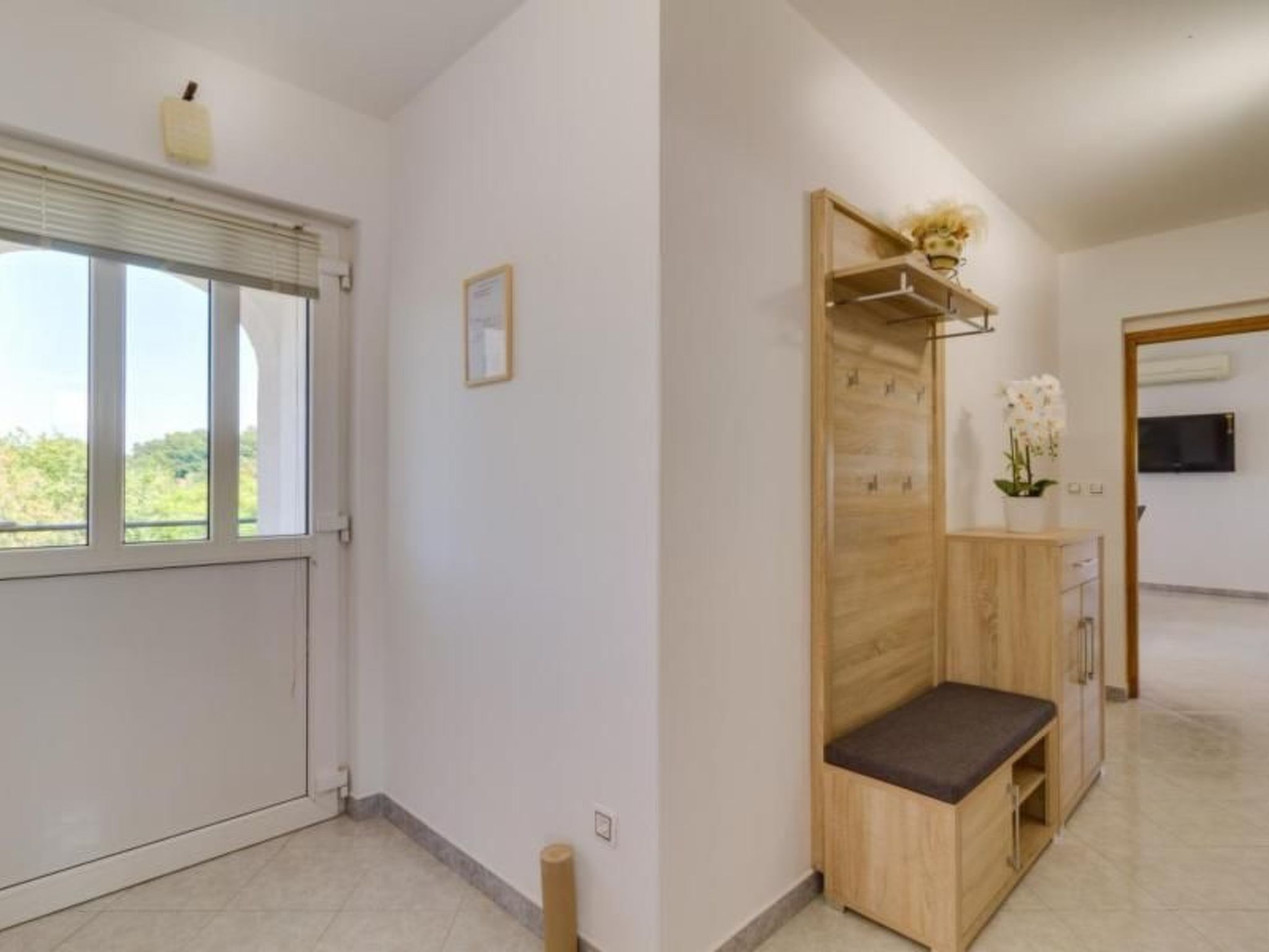 Ein Hotelzimmer mit großem Fenster, einer Holzbank, einem kleinen Tisch mit Blumenvase und einem an der Wand befestigten Fernseher.