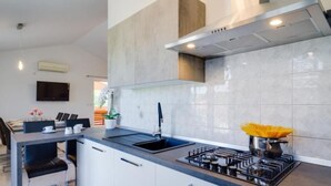 A modern kitchen with a gas stove, a sink, and a dining area with a table and chairs. - "Haus Piljan" by Interhome (Bokordici)