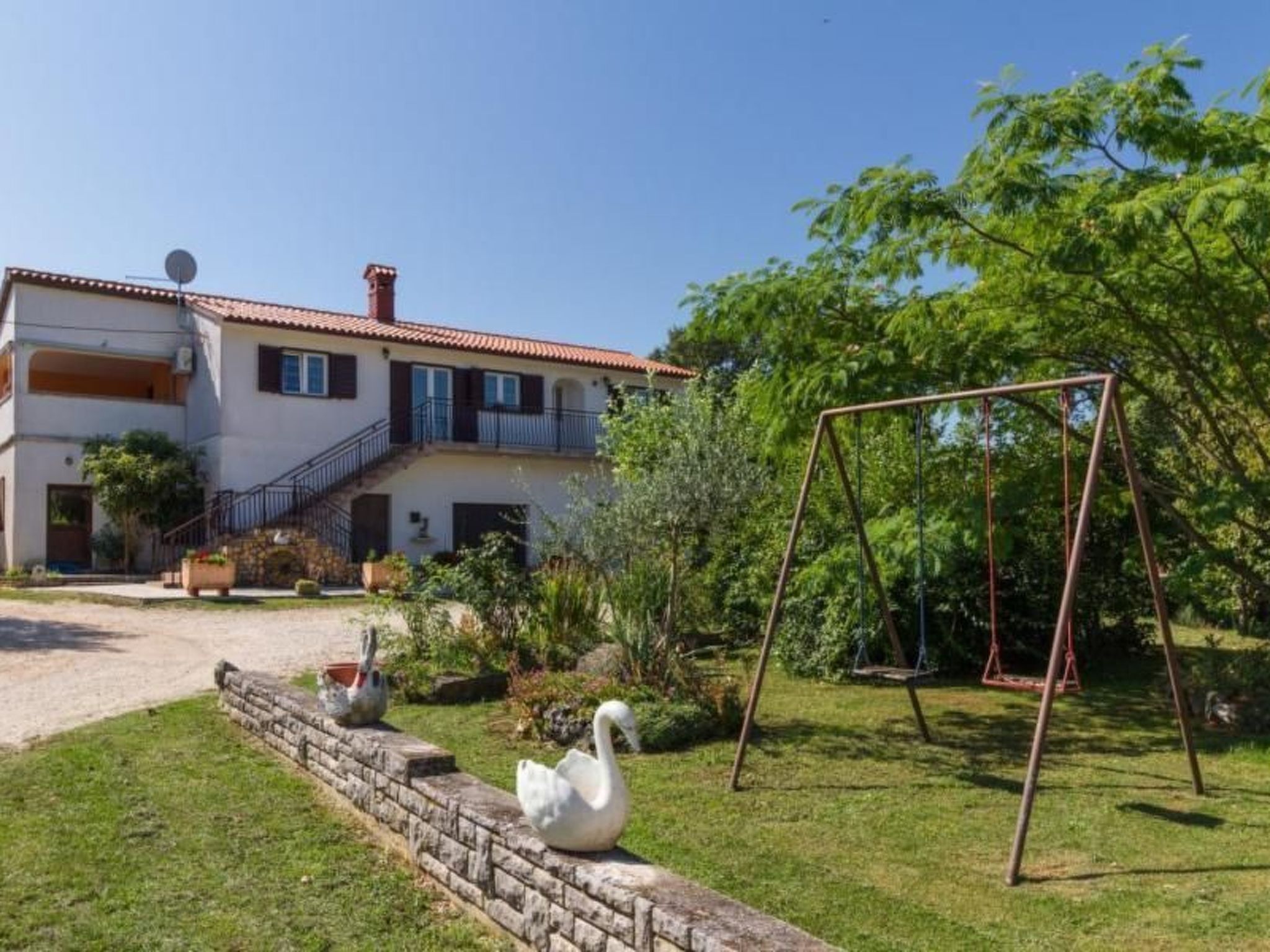 A two-story house with a red-tiled roof, a balcony, and a swing set in the yard.
