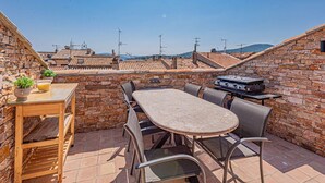 Terrassa al terrat amb taula, cadires, una barbacoa i plantes en testos.