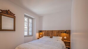 Un dormitori amb un llit gran, un capçal de fusta, una petita taula de nit, una làmpada penjada a la paret i una finestra amb vistes a l'exterior.