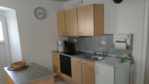 Cocina compacta con armarios de madera, horno empotrado, pileta y un refrigerador pequeño.