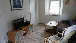 Una sala de estar con televisor, estantería, ventana y sofá.