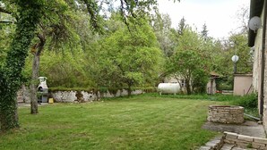 Un patio trasero con césped, un muro de piedra, un tanque cilíndrico blanco y un pozo de piedra.