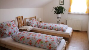 Un dormitori amb dos llits individuals, cadascun amb roba de llit floral, un capçal de fusta i una taula de nit amb una làmpada. Hi ha una planta en test amb un suport al costat de la paret, i una finestra amb cortines.