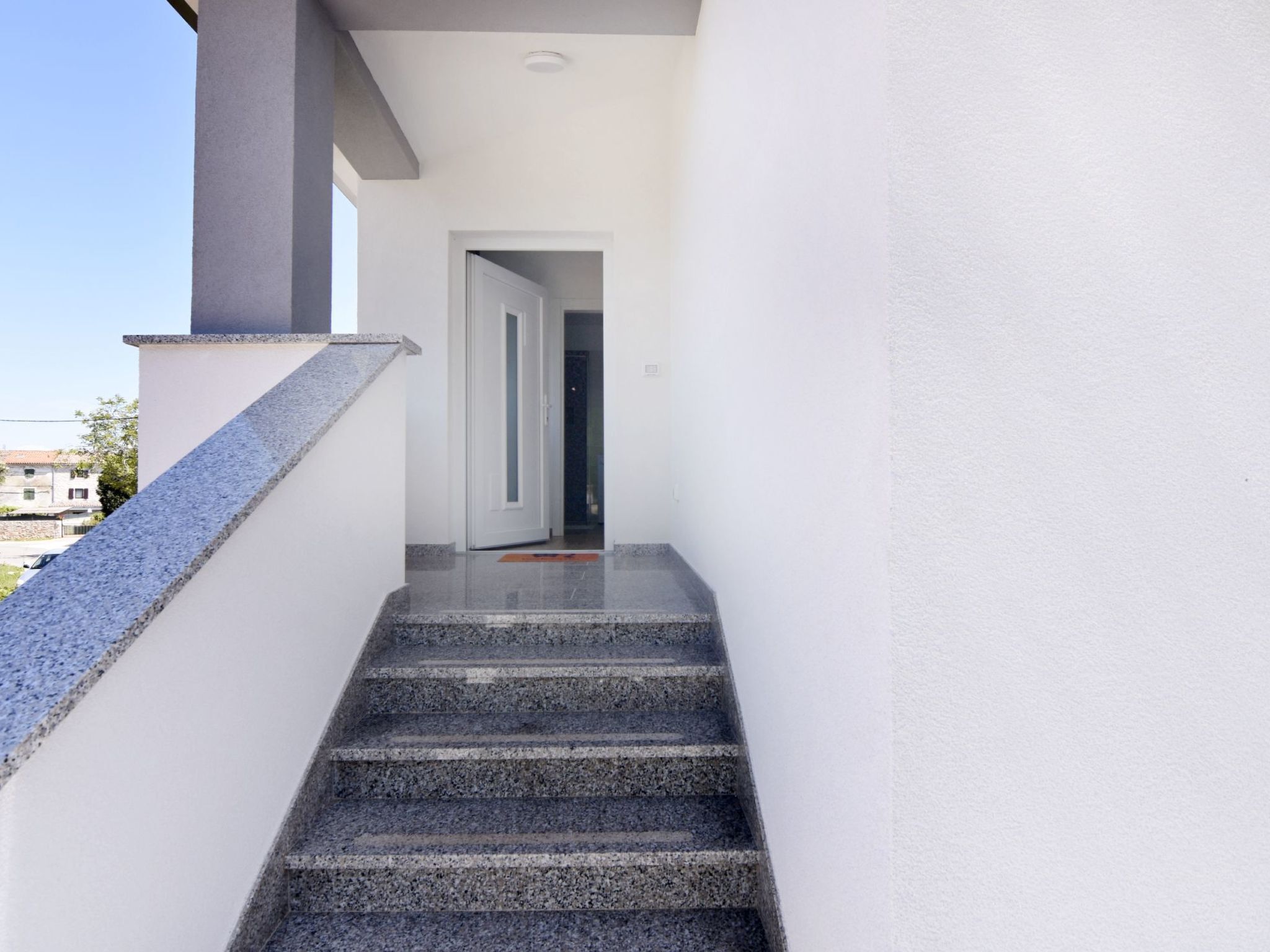 Un escalier menant à une porte, avec un mur blanc d’un côté et un mur gris de l’autre.