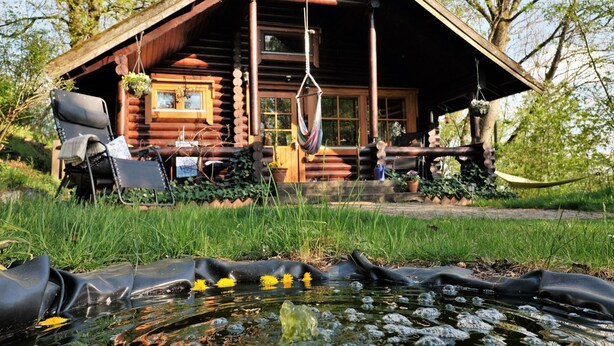 Eine Blockhütte mit Veranda, einer Hängematte und einem kleinen Teich mit gelben Blumen.