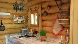 Eine Holzhüttenküche mit einer gefliesten Spritzschutzwand, einem Spülbecken, einem Herd und verschiedenen Küchenutensilien, die an der Wand hängen.