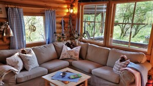Ein gemütliches Blockhaus-Interieur mit Holzvertäfelung, einem beigen Sofa, einem kleinen Holztisch und großen Fenstern mit Blick auf Bäume.