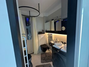A modern bathroom with a built-in washing machine, a shower with a black ceiling light, and a large mirror above the sink. - Wohnung Fiorino Rijeka, Kvarner Bucht by Interhome (Rijeka)