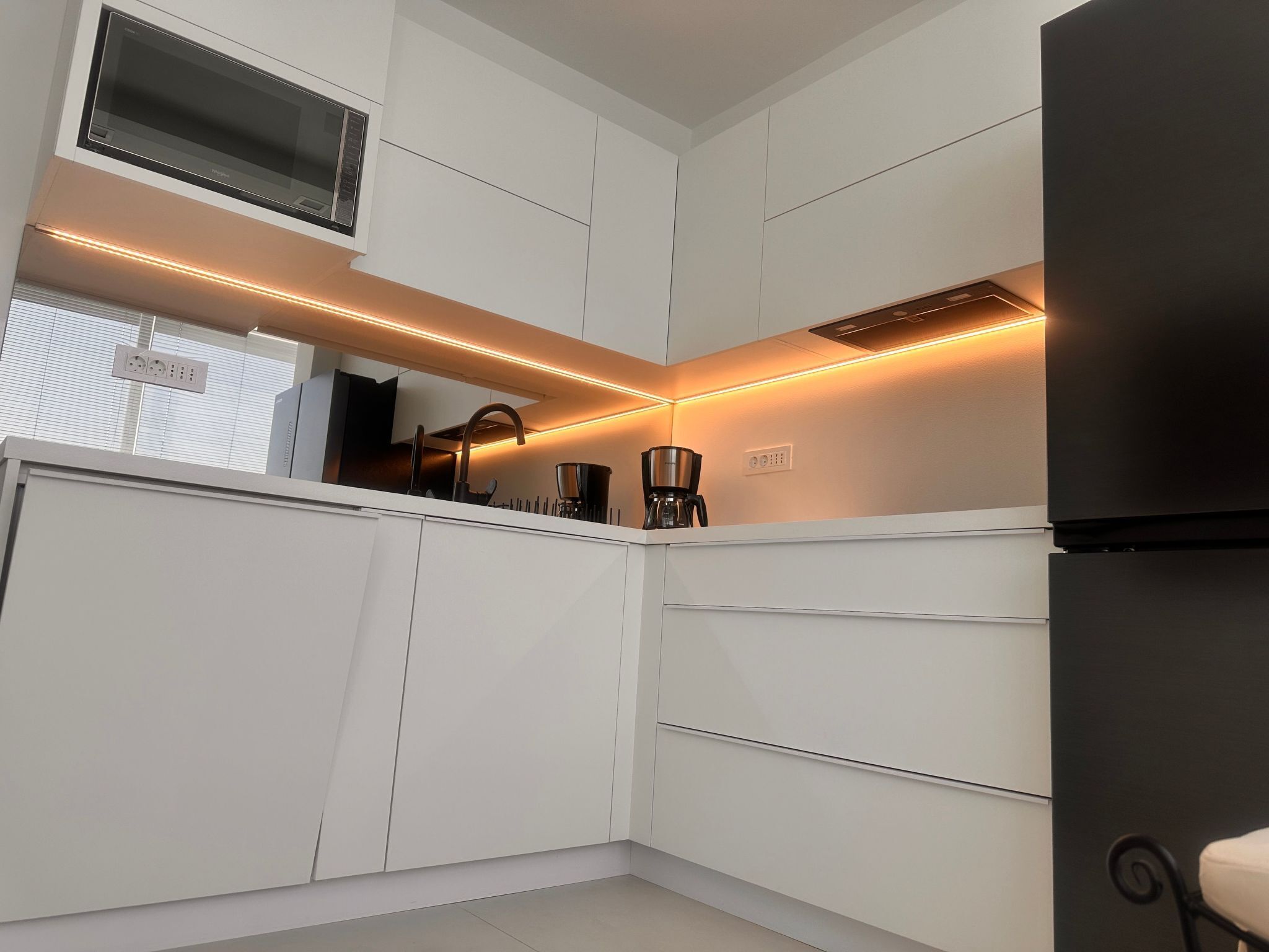 A modern kitchen with white cabinetry, a built-in microwave, a coffee maker, and under-cabinet lighting.