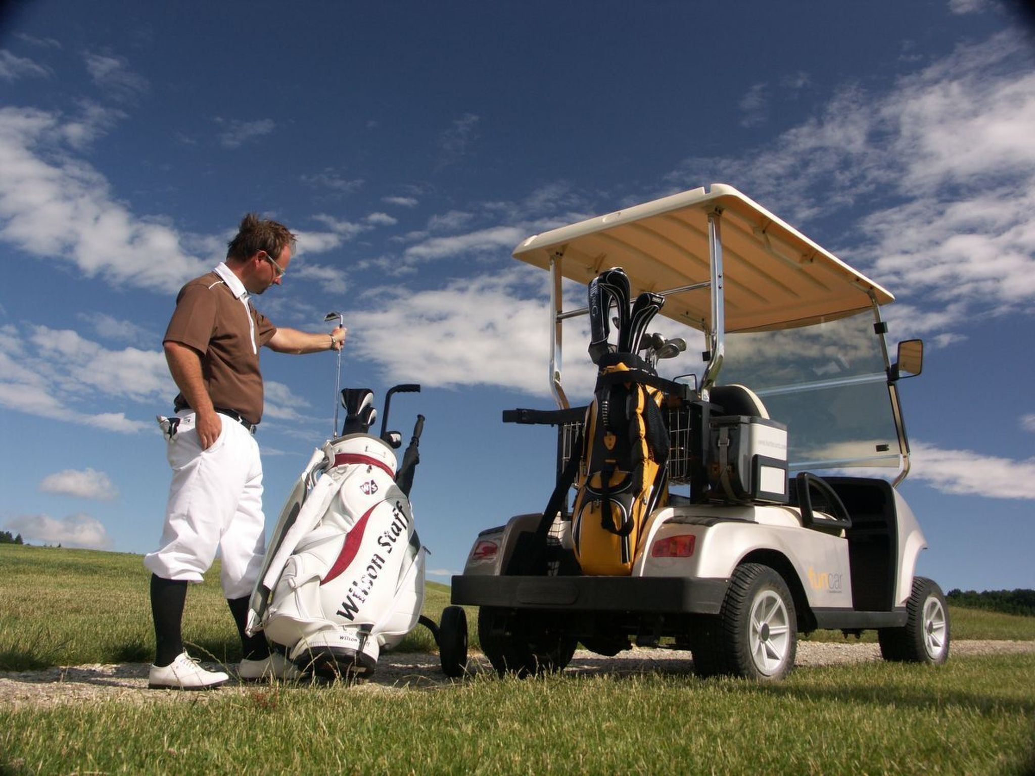 A golf cart with a golf bag and a person standing beside it.