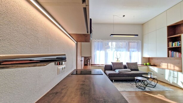 Eine moderne Küche mit Einbauherd, ein Essbereich mit Tisch und Stühlen sowie ein Wohnzimmer mit Sofa und Couchtisch.