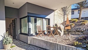 Ein moderner Außenbereich zum Sitzen mit einer Steinwand, einem Holztisch und zwei Holzstühlen.