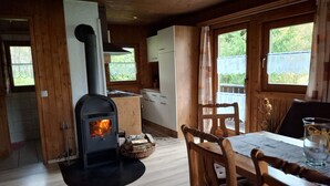 Ein gemütliches Blockhaus-Interieur mit Kaminofen, Holzmöbeln und großen Fenstern mit Blick auf Grünflächen.