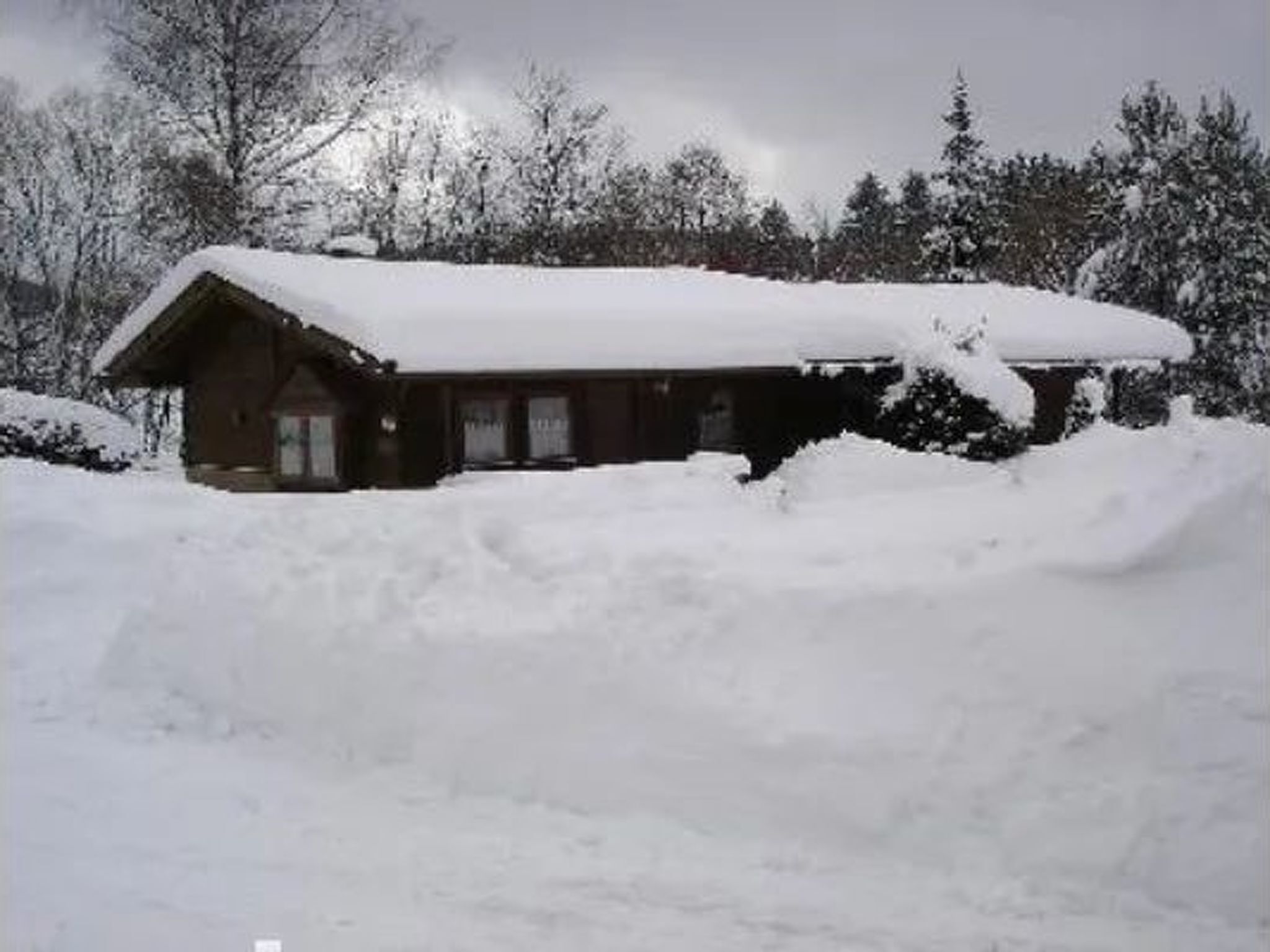 Une cabane dont le toit et les murs sont recouverts de neige, entourée d’arbres et d’un paysage enneigé.