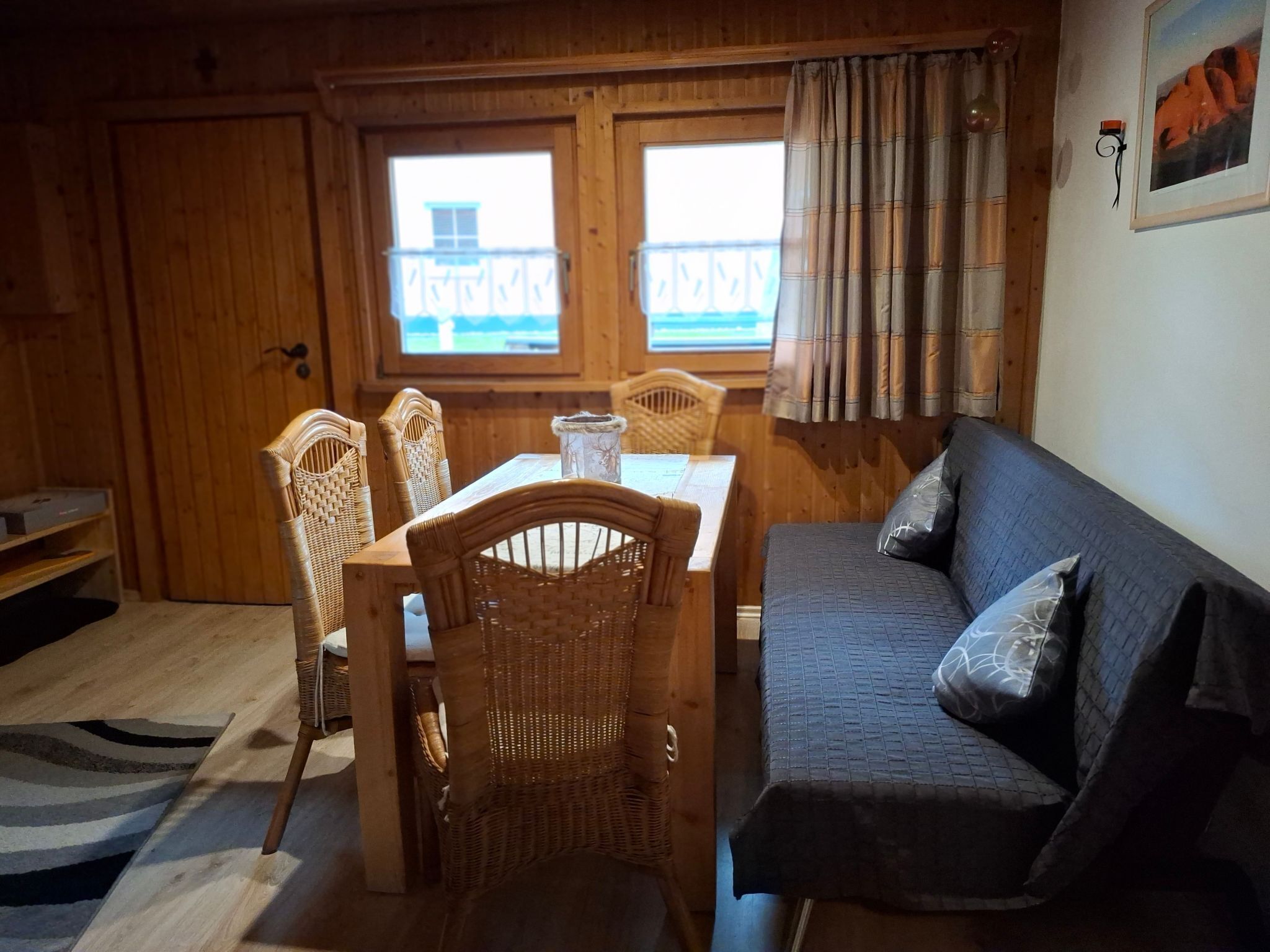 Ein gemütliches Zimmer mit Holzvertäfelung, einem Esstisch mit Stühlen, einer Couch und einem Fenster mit Aussicht.