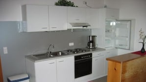 A compact kitchen with white cabinets, a stainless steel sink, a coffee maker, and a wooden countertop. - Apartment Gottal by Interhome (Neuschönau)