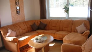 A living room with a large L-shaped orange sofa, a coffee table, and a vase with flowers on a windowsill. - Apartment Gottal by Interhome (Neuschönau)