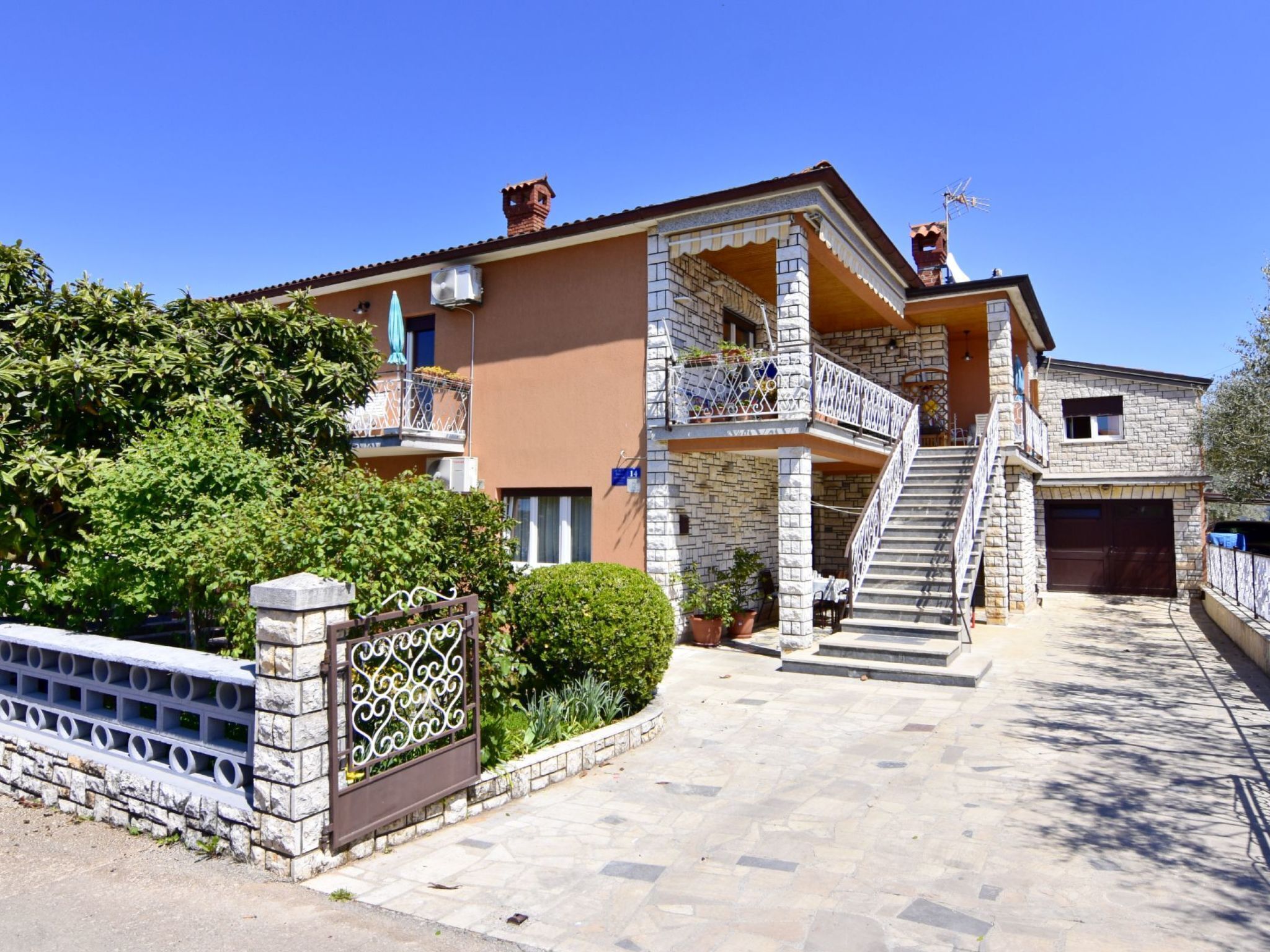 Ein zweistöckiges Haus mit Naturstein-Fassade, einem Balkon mit Metallgeländern und einer Treppe, die zum Obergeschoss führt.