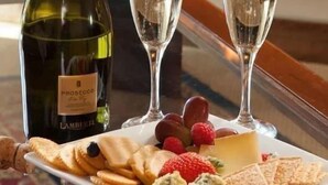 A bottle of Prosecco, two glasses of wine, and a plate with crackers, cheese, and grapes on a table. - THE DEEP GANESHA INN (New Delhi)