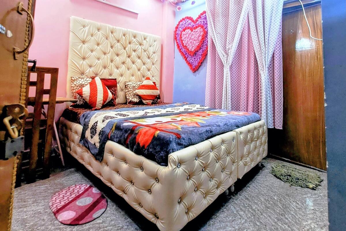 A bedroom with a tufted headboard, a bed with a floral bedspread, a ceiling fan, and decorative heart-shaped wall art.