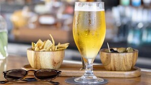 A bar setting with a glass of beer, wooden bowls of snacks, and a pair of glasses on a wooden table. - THE DEEP GANESHA INN (New Delhi)