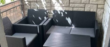 A patio area with a stone wall, a dark-colored sofa, and a matching table.