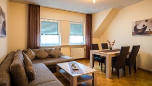 Una sala de estar con un sofá seccional, una mesa de comedor con sillas y un piano.