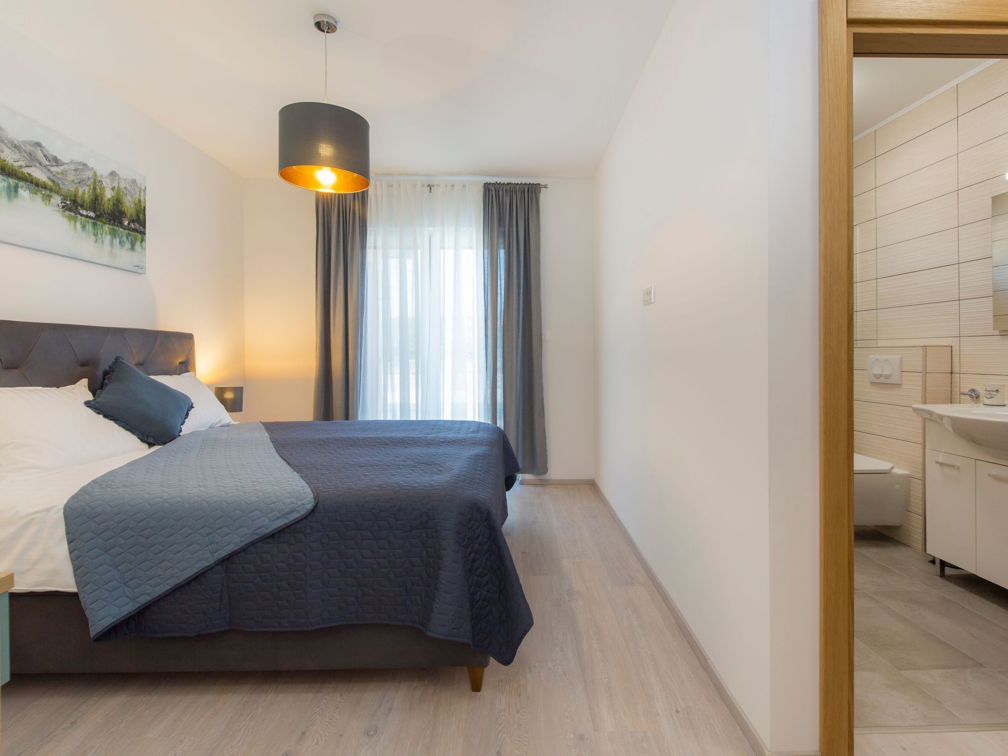 A modern bedroom with a bed, a bedside lamp, a painting, and a view of a bathroom.