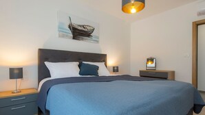 Een moderne slaapkamer met een groot bed, twee nachtkastjes, een wandlamp en een lijst met een afbeelding van een boot.