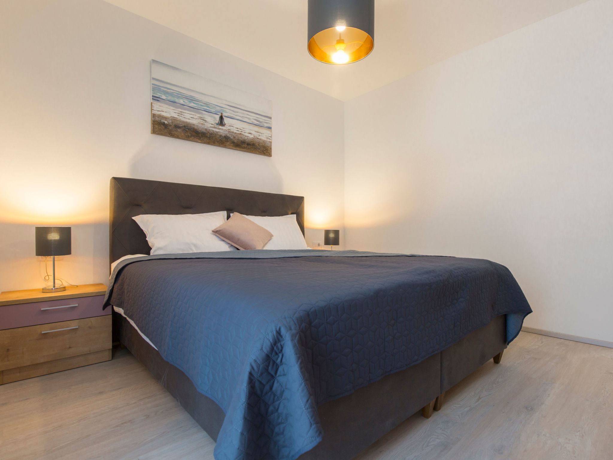 A bedroom with a bed, bedside tables, and a painting on the wall.