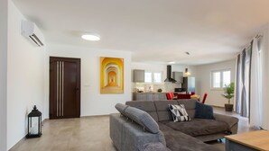 Een moderne woonkamer met een grijze hoekbank, een houten salontafel en een keuken op de achtergrond.