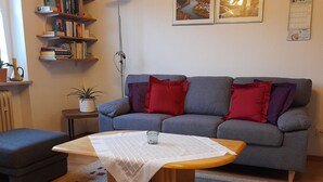 A living room with a grey sofa, red and purple cushions, a small side table with a plant, and a coffee table with a white tablecloth. - Fe.Wo.Renate Ebach by Interhome (Alf)