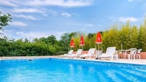 Una piscina con sillas de descanso blancas y sombrillas rojas.