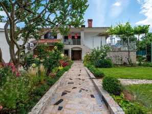 A two-story house with a stone pathway leading to the entrance, surrounded by lush gardens and a tree. - Apartment Vinez by Interhome (Drenje)