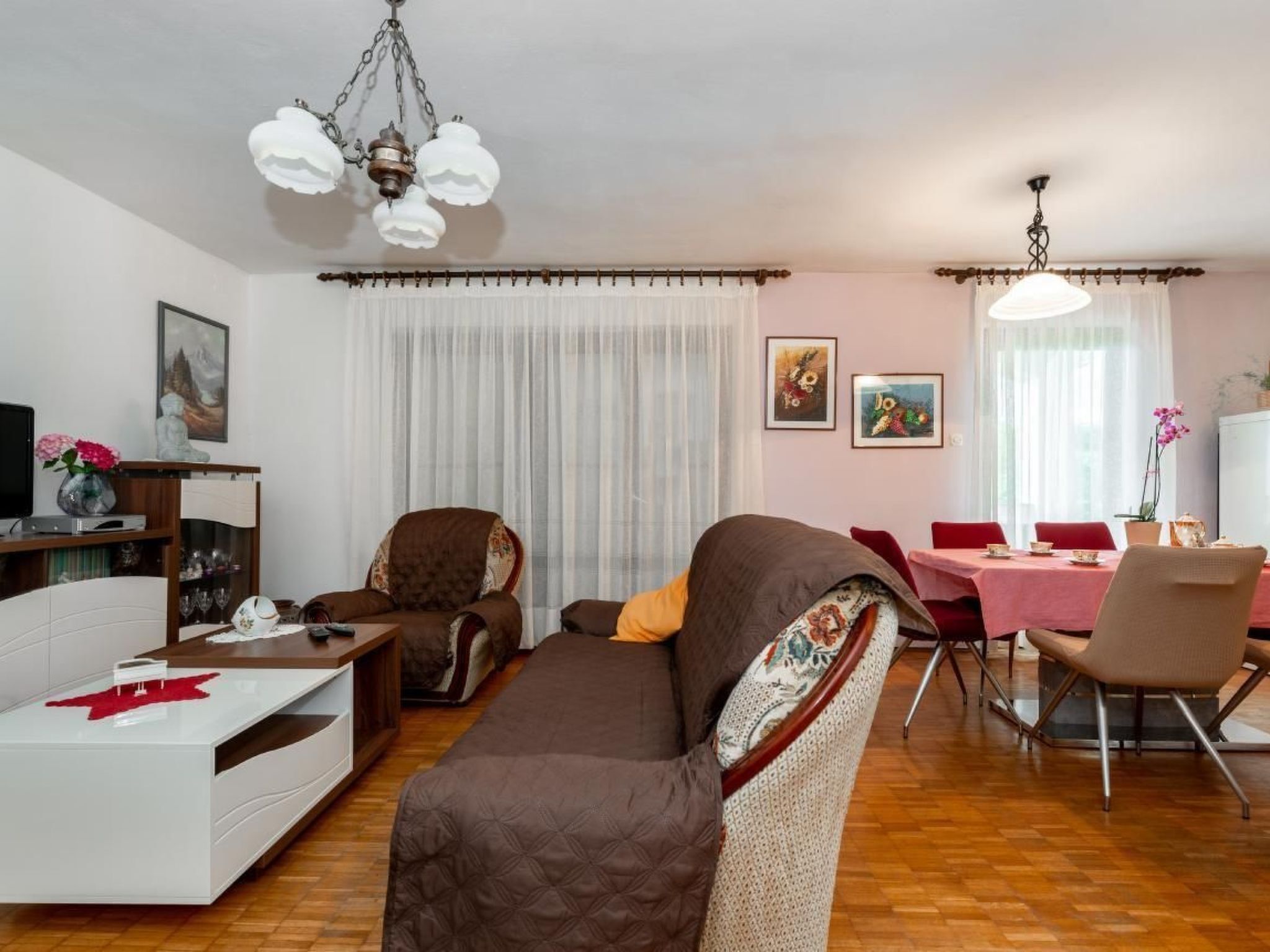 Ein Wohnzimmer mit einer Couch, Sesseln, einem Esstisch mit Stühlen, einem Fernseher und Kunstwerken an den Wänden.
