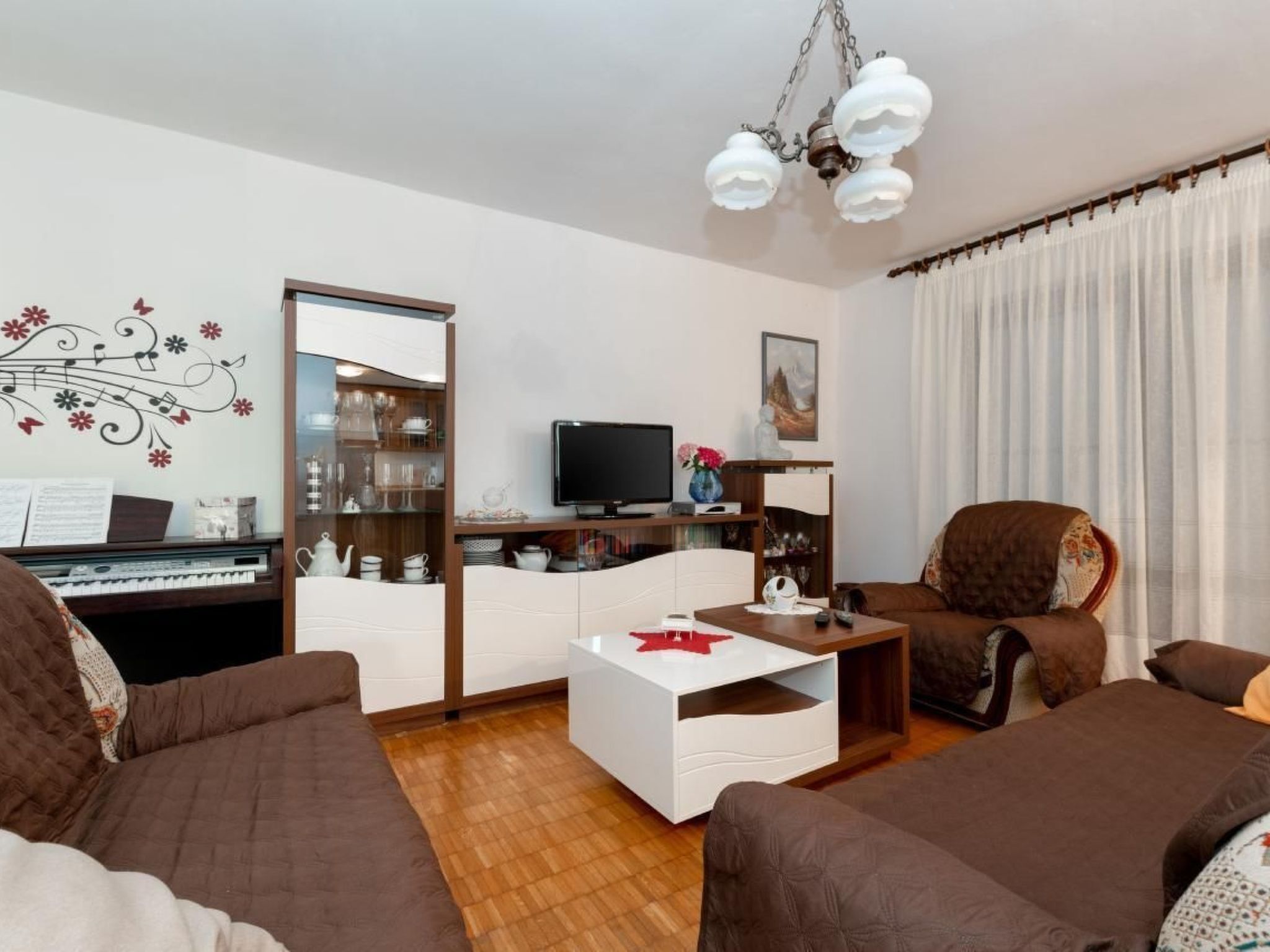 A living room with a piano, a television, a white cabinet, and a brown armchair.