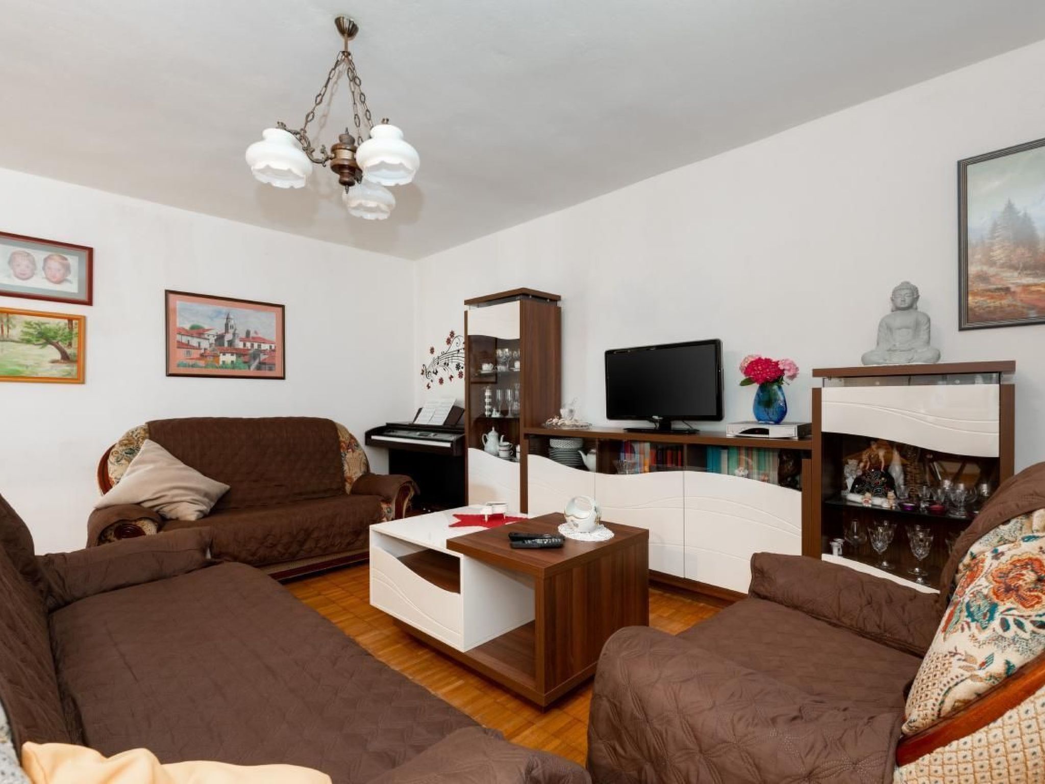 A living room with brown sofas, a coffee table, a TV, and a piano.