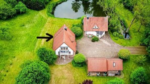 Luftaufnahme einer Anlage mit zwei Hauptgebäuden, einem Teich und umgebender Bepflanzung.