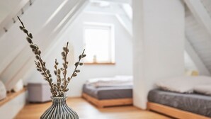 Ein modernes Schlafzimmer im Loft-Stil mit schrägem Dach, einem Bett mit Holz-Kopfseitenverkleidung und einer Tischvase mit Zweigen auf einem weißen Tisch.