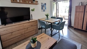 A modern living room with a flat-screen TV, wooden furniture, and a dining area with blue chairs. - Summer escape Rovinj by Interhome (Rovinj)