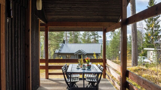 Une terrasse en bois avec une table et des chaises, d’où l’on peut admirer une maison dont le toit est recouvert de tuiles.