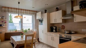 Cocina compacta con comedor, que incluye un ventanal con cortinas, cafetera y estufa.