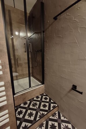 A bathroom with a glass shower enclosure, a tiled floor with a geometric pattern, and a textured wall. - Möwennest by DeJu by Interhome (Norderney)