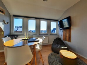 A modern living room with a dining area, large windows, a flat-screen TV, and a cozy seating arrangement. - Möwennest by DeJu by Interhome (Norderney)