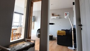 Sala moderna com um banco de madeira, um sofá e uma área de jantar visível por uma porta aberta.