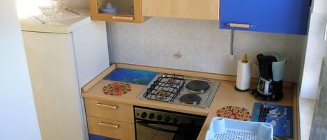 A compact kitchen with a gas stove, oven, and a sink. There is a coffee maker and a dish rack on the countertop.